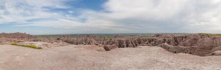 Tourists take in a panoramic view of dramatic mountain formations carved out by erosion showing layers of rocks with spring wildflowers below in Badlands National Park, South Dakota.の写真素材