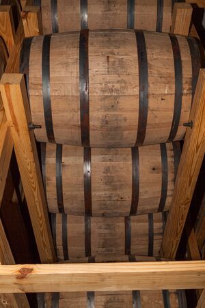 Whiskey barrels full of alcohol are stacked into a wooden holding rack so the bourbon inside can...