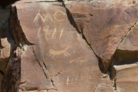 Modern graffiti that is over a hundred years old on a sandstone rock with a small petroglyph carving...