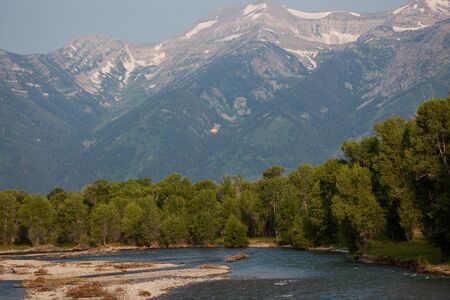 A colorful hot air balloon looks tiny when compared to its surrounding of the Grand Teton mountains and the Snake River in Wyoming.の写真素材