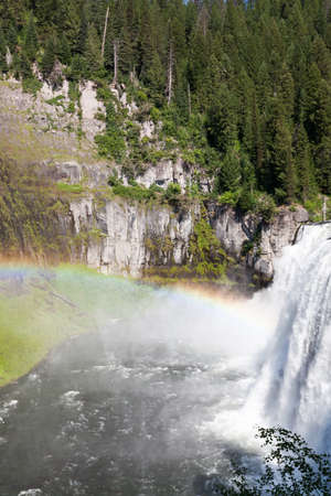 A rainbow in the mist of Upper Mesa Falls as it cascades over a cliff in the rugged wilderness of Henrys Fork of the Snake River along the Mesa Falls Scenic Byway in Idaho.の写真素材