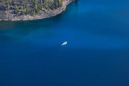 A tour boat takes people around the the magnificently blue and deep Crater Lake next to the edge of...