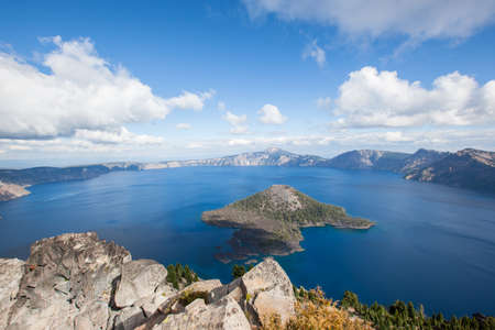 A dramatic high elevation view of the deep blue Crater Lake and Wizard Island from Watchman Tower on the Western rim with white fluffy clouds in late summer.の写真素材