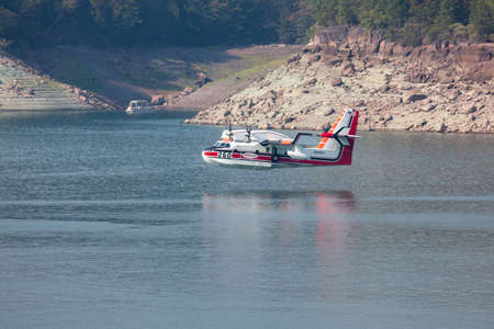 Lost Creek Lake near Prospect,  Oregon / USA - September 7, 2014:  A small fire fighting plane prepares to scoop water as it comes in low over the lake with a boat in the background at Lost Creek Lake near Prospect, Oregon.のeditorial素材