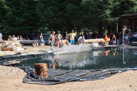 Prospect, Oregon / USA - August 16, 2014: Volunteers roll a log into a pond with a splash for a skill competition at the Prospect Hillbilly Jamboree and Timber Carnival in Prospect, Oregon.のeditorial素材