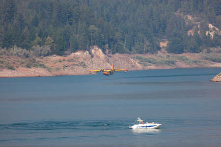 Lost Creek Lake near Prospect,  Oregon / USA - September 7, 2014:  A small fire fighting plane prepares to scoop water as it comes in low next to a boat and downed waterskier at Lost Creek Lake near Prospect, Oregon.のeditorial素材