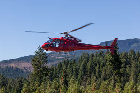 Prospect,  Oregon / USA - September 9, 2014:  A red fire fighting helicopter takes off from Prospect State Airport with a hanging rope and bucket to help put out the 790 Fire near Prospect, Oregon.のeditorial素材