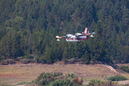 Lost Creek Lake near Prospect,  Oregon / USA - September 7, 2014:  A small fire fighting plane prepares to scoop water as it comes in low over a mountain in a smoke filled sky at Lost Creek Lake near Prospect, Oregon.のeditorial素材