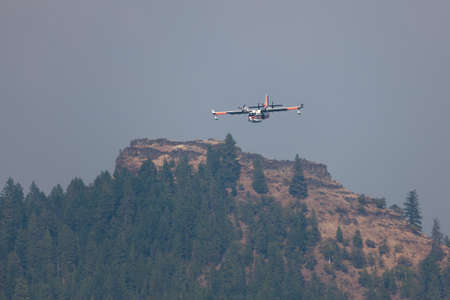 Lost Creek Lake near Prospect,  Oregon / USA - September 7, 2014:  A small fire fighting plane prepares to scoop water as it comes in low over a mountain in a smoke filled sky at Lost Creek Lake near Prospect, Oregon.のeditorial素材