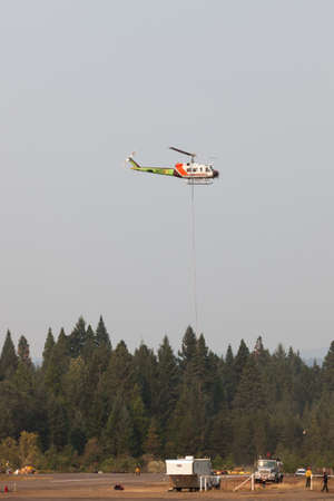 Prospect,  Oregon / USA - September 13, 2014:  A fire fighting helicopter takes off in a smoke filled sky from Prospect State Airport with a hanging rope and bucket to help put out the 790 Fire near Prospect, Oregon.のeditorial素材