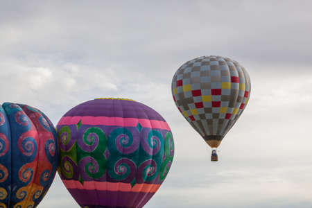 Two bright hot air balloons tough each other as they prepare to take off with checkered balloon rising in the distance.の写真素材