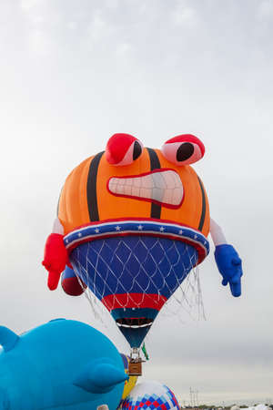 A hot air balloon that looks like a basketball with a face being squeezed into a basket with a net and a grimace on its face at the Balloon Fiesta in New Mexico.の写真素材