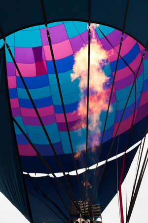 A bright flame rising up into the interior of a colorfully patterned hot air balloon at the Balloon Fiesta in New Mexico.の写真素材