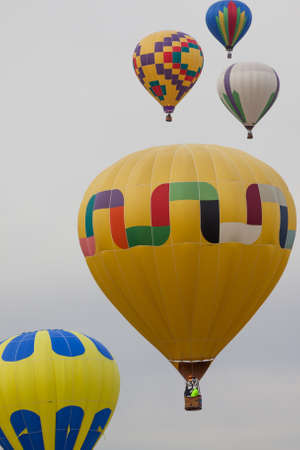 A group of colorful hot air balloons rising up into the cloudy morning sky at the Balloon Fiesta in New Mexico.の写真素材