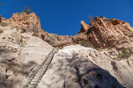 A wooden ladder leads up to a cave opening carved into a sandstone cliff by the Pueblo people in Frijoles Canyon located in Bandelier National Monument, New Mexico.の写真素材