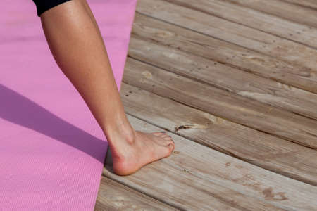 The lower leg and foot of a woman who is getting ready to do yoga with a pink mat outside on a...