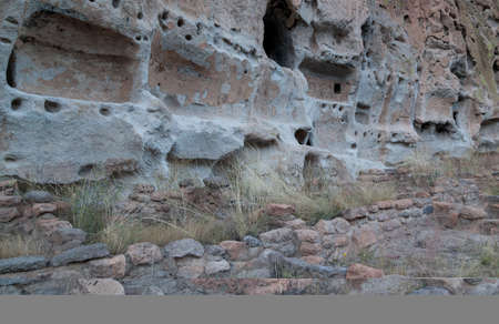 A foundation of brick and clay still stands where a tall building used to be that butted up against sandstone walls with cave openings in Frijoles Canyon, part of Bandelier National Monument in New Mexico.の写真素材