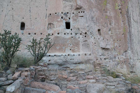A foundation of brick and clay still stands where a tall building used to be that butted up against sandstone walls with cave openings in Frijoles Canyon, part of Bandelier National Monument in New Mexico.の写真素材