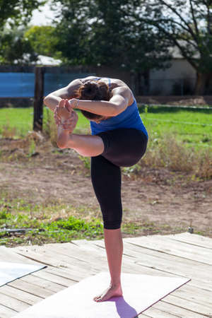 A yoga instructor holds an intricate pose of flexibility and balance at an outdoor afternoon yoga class at a farm.の写真素材