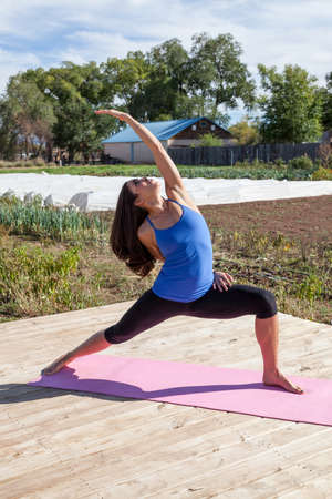 A yoga instructor holds an intricate pose of flexibility and balance at an outdoor afternoon yoga class at a farm.の写真素材