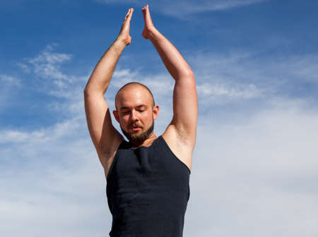 A man doing a yoga pose on a sunny afternoon with bright sunshine and a background of blue sky and wispy clouds.の写真素材