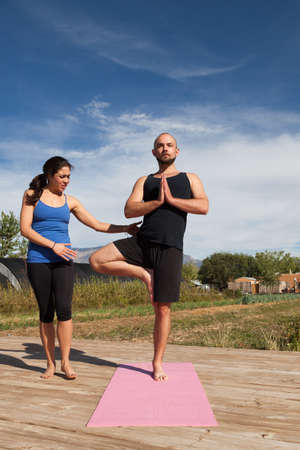 A yoga instructor gives tips to students at an outdoor afternoon yoga class that is held on a wooden platform at a farm.の写真素材