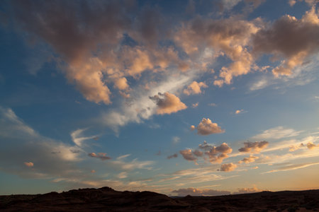 The setting sun turns low fluffy clouds pink over Glen Canyons Horseshoe Bend landscape in Northern Arizona.の写真素材