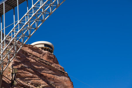The circular Carl Hayden Visitor Center sits on red sandstone cliffs high above the Glen Canyon Dam and Lake Powell with the steel arch tresses of the Glen Canyon Bridge close by.の写真素材