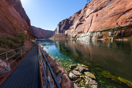 Looking down a walkway to the Colorado River and a group of tourists preparing to take a rafting trip through the red walls of Glen Canyon.の素材 [FY310162519781]