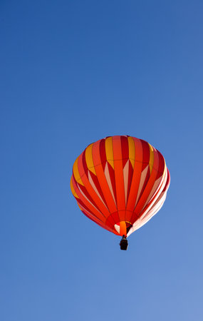 A colorful hot air balloon floating up into the clear blue sky with bright sunshine on the side in Page, Arizona.の写真素材
