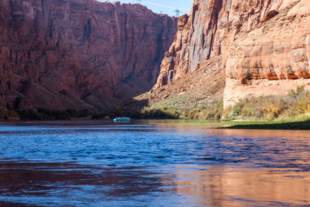A blue rubber raft floats down the Colorado River through Glen Canyon with bright sunshine reflecting off the surface of the water.の写真素材
