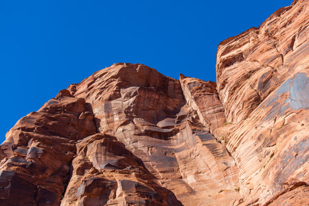 The towering red sandstone walls of Glen Canyon with several cracks through the aged rock lit by bright sunshine and topped with brilliant blue sky.の写真素材