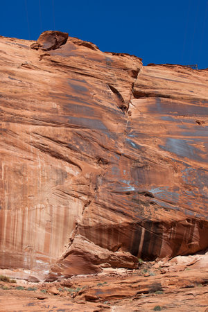 The towering red sandstone walls of Glen Canyon with a massive crack running from top to bottom and lit by bright sunshine.の写真素材