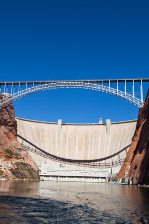 The Glen Canyon Dam holding back Lake Powell and the Glen Canyon Bridge with a clear blue sky background as seen from the surface of the Colorado River near Page, Arizona.の写真素材