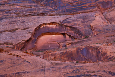 Eroding sandstone canyon walls creating an arch pattern with newer bright sandstone exposed in the arch, and dark patina on the older sandstone surrounding it.の写真素材