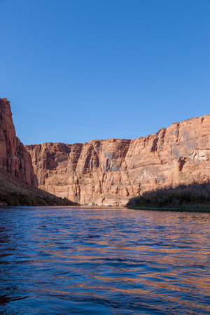 Morning in the Glen Canyon with shadow on the Colorado River and bright sunshine on the Western canyon wall against a clear blue sky.の写真素材