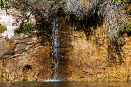 A small stream of water cascades down a sandstone wall inside of Glen Canyon and joins with the mighty Colorado River on a sunny day.の写真素材