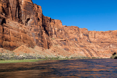 The inside of Glen Canyon as seen from the surface of the Colorado River with brightly lit sandstone walls and a clear blue sky.の写真素材