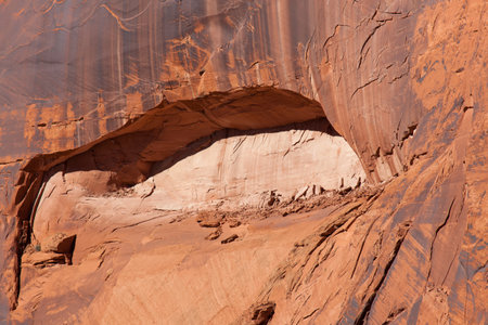 Eroding sandstone canyon walls creating an arch pattern with newer bright sandstone exposed in the arch, and dark patina on the older sandstone surrounding it.の写真素材
