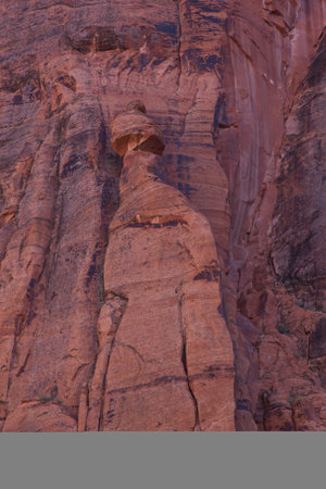 A tall hoodoo tower next to the sandstone walls of Glen Canyon with a broken but balanced top hat that is waiting for the right conditions to fall.の写真素材