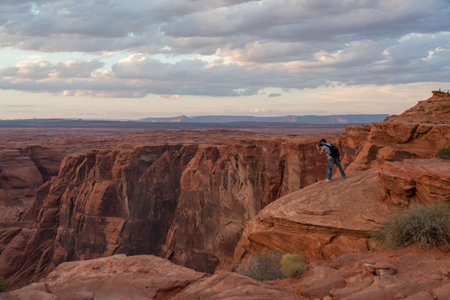 Horseshoe Bend, Arizona / USA - October 25, 2014:  A man stands of the edge of a cliff at Horseshoe Bend near Page, Arizona at sunset to take pictures of the Colorado River below.のeditorial素材