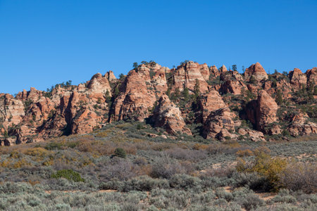 A ridge of red layered sandstone that has been eroded over time to create unique shapes that are dotted with trees and brush near Zion National Park, Utah.の写真素材