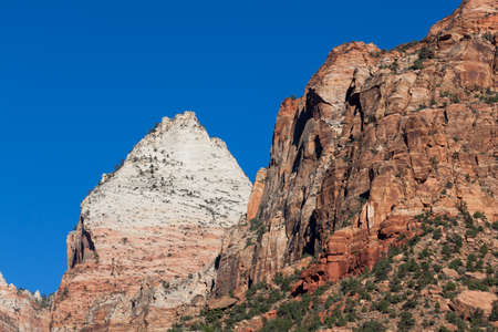High dramatic cliffs with red, orange and white sandstone layers and a vibrant clear blue sky in Zion National Park, Utah.の写真素材