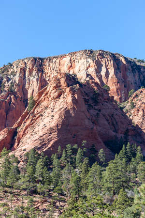 A ridge of red layered sandstone that has been eroded over time to create unique shapes that are dotted with trees and brush near Zion National Park, Utah.の写真素材