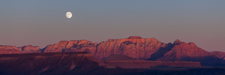 The full moon rising over the dramatic mountains of Zion National Park lit by the setting sun with a clear sky.の写真素材