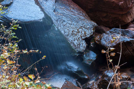 A small waterfall looks like rain falling onto the massive boulders at Emerald Pool in Zion National Park, Utah.の写真素材