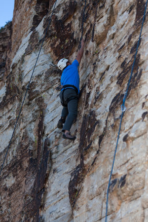 A rock climber reaching up for the next hand hold as he  climbs straight up a sandstone rock cliff in Southern Utah.の写真素材