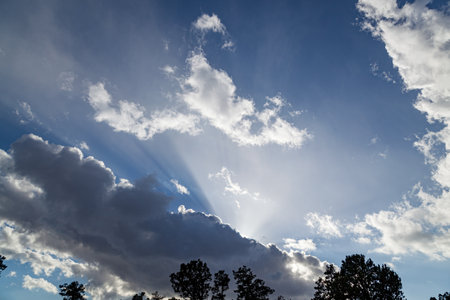 Afternoon sunlight from behind storm clouds creating a bright beam of light reflecting up into the blue sky in a display of celestial beauty.の写真素材