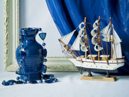 Sailing vessel and vase with a beads against a blue and a whiteの写真素材