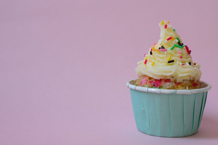 A cupcake with butter cream frosting and colorful sprinkles on pink background.の写真素材